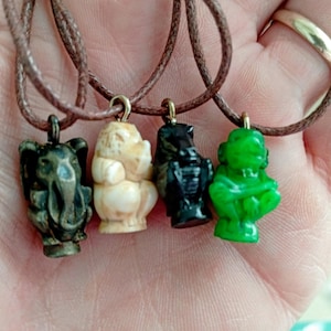 May include: Four animal pendant necklaces. The pendants are a dark grey elephant, a cream-colored hippo, a black hippo, and a green frog. Each pendant is attached to a brown cord necklace.