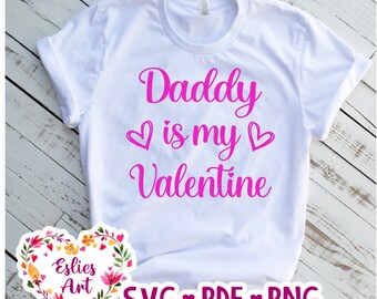 May include: White t-shirt with pink text that reads "Daddy is my Valentine" with two pink hearts.  The shirt is on a wood background.  A floral heart graphic with the text "Eslies Art" is in the lower left corner.  The text "SVG ♥ PDF ♥ PNG" is in the lower right corner.