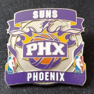 May include: A purple, silver, and gold metal pin with the Phoenix Suns logo. The logo features a basketball with the words "PHX" and "Phoenix Suns" on it. The basketball is surrounded by flames.