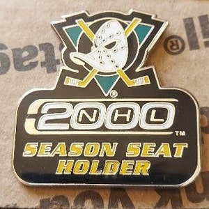 May include: A black and gold pin with the Anaheim Ducks logo and the text "NHL 2000 Season Seat Holder".