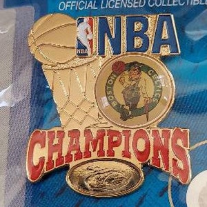 May include: Gold NBA Champions pin with a basketball hoop, a Boston Celtics logo, and the words "NBA Champions".