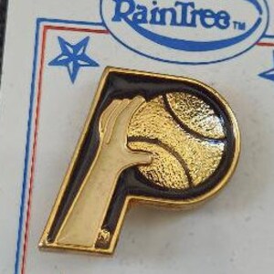 May include: Gold-colored pin featuring a stylized letter 'P' with a basketball and a hand reaching for the ball. The pin is black and gold with a white hand.
