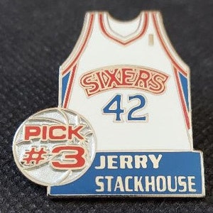 May include: A white basketball jersey with the word "SIXERS" in red and blue letters, the number "42" in blue, and the name "JERRY STACKHOUSE" in blue on a blue background. A basketball with the words "PICK #3" is in the lower left corner.