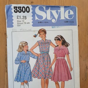 May include: A sewing pattern for a girl's dress. The pattern shows three girls wearing different styles of dresses. The pattern number is 3300 and the price is £1.25. The pattern is for size 12, with a 76 cm bust.