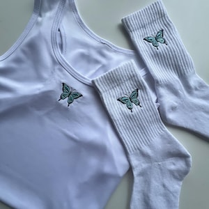 May include: White tank top and socks with embroidered blue butterflies. The tank top has a scoop neck and the socks are crew socks.