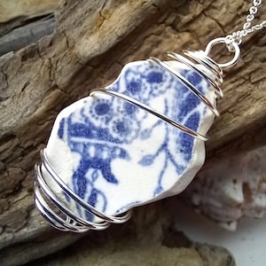 May include: A silver wire wrapped pendant necklace featuring a blue and white ceramic shard with a floral pattern.