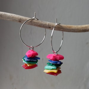 May include: A pair of silver hoop earrings with colourful plastic charms hanging from them. The charms are stacked and include pink, blue, green, and yellow.