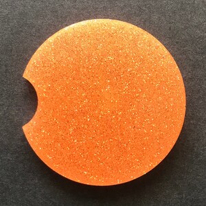 K&ouml;nnte beinhalten: Runder Untersetzer aus orangefarbenem Glitzer mit einer Aussparung f&uuml;r eine Tasse. Der Untersetzer hat eine glitzernde Oberfl&auml;che.