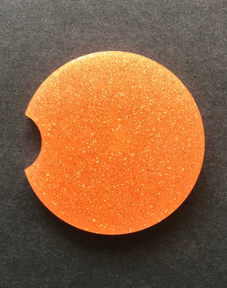K&ouml;nnte beinhalten: Runder Untersetzer aus orangefarbenem Glitzer mit einer Aussparung f&uuml;r eine Tasse. Der Untersetzer hat eine glitzernde Oberfl&auml;che.