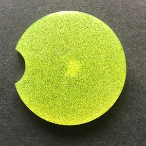 K&ouml;nnte beinhalten: Ein runder, gelb-gr&uuml;ner Glitzer-Untersetzer mit einer Aussparung f&uuml;r eine Tasse.