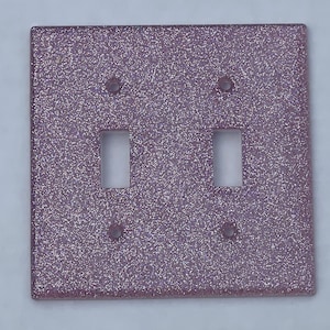 May include: A double light switch plate with a glittery, iridescent purple finish. The plate has two rectangular cutouts for the switches and four small holes for mounting screws.