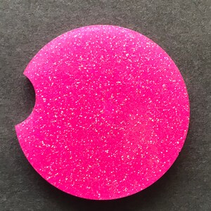 K&ouml;nnte beinhalten: Ein runder Untersetzer aus pinkfarbenem Glitzer mit einer Aussparung f&uuml;r eine Tasse. Der Untersetzer hat eine glitzernde Oberfl&auml;che.