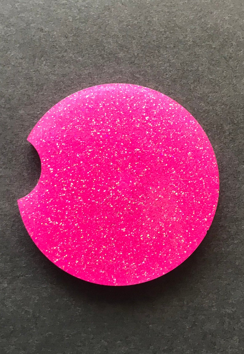K&ouml;nnte beinhalten: Ein runder Untersetzer aus pinkfarbenem Glitzer mit einer Aussparung f&uuml;r eine Tasse. Der Untersetzer hat eine glitzernde Oberfl&auml;che.