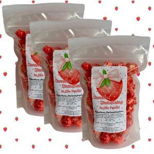 May include: Four clear plastic bags filled with red strawberry flavored popcorn. Each bag has a label with a strawberry graphic and the text "Sweetest Strawberry in the Patch!". The bags are sealed and ready to eat.