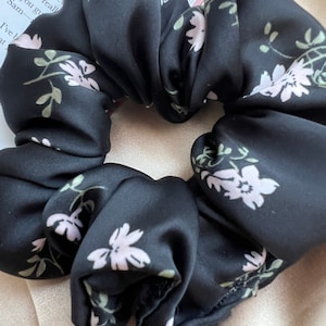 May include: A black satin scrunchie with a floral pattern. The flowers are pink and white with green leaves.