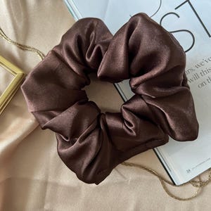 May include: A brown satin scrunchie hair tie. The scrunchie is made of soft, silky fabric and is perfect for adding a touch of elegance to any hairstyle.