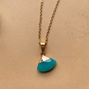 Puede incluir: Un collar de cadena dorada con un colgante de piedra preciosa azul verdoso en forma de abanico.