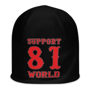 Op de afbeelding: Zwarte beanie met de tekst "SUPPORT 81 WORLD" in rode letters met een grijze rand. Een warme, gebreide muts, ideaal voor koudere temperaturen. De tekst is duidelijk zichtbaar.