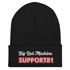 Op de afbeelding: Zwarte gebreide beanie met witte geborduurde tekst "Big Red Machine" en rode geborduurde tekst "SUPPORT81".