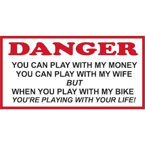 May include: A red and white sign with the word "DANGER" in large red letters. The sign reads "You can play with my money, you can play with my wife, but when you play with my bike you're playing with your life!"