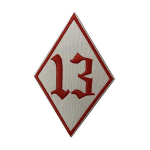 May include: A diamond-shaped patch with a white background and a red border. The number "13" is embroidered in red gothic font in the center of the patch. This patch is suitable for jackets, bags, or other apparel.