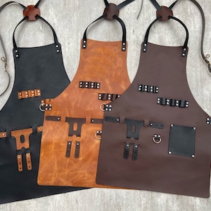 May include: Three leather aprons with adjustable straps and multiple pockets. The aprons are black, brown, and dark brown.