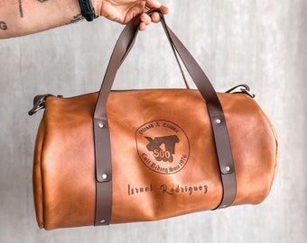 May include: A brown leather duffel bag with a brown leather strap. The bag has a circular logo with the text "Old Road & Classic", "C.U.L.L. Riding Since 1976", and "500". The bag is personalized with the name "Israel Rodriguez".