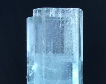 May include: A clear, light blue aquamarine crystal with a rectangular shape. The crystal has a smooth, polished surface and is translucent.