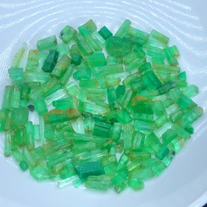 May include: A collection of raw emerald crystals in various sizes and shapes. The crystals are a vibrant green color and have a natural, rough texture.