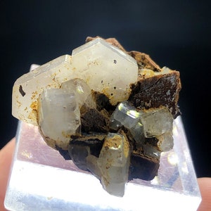 May include: A cluster of clear, translucent crystals with a brown, earthy matrix. The crystals have a slightly iridescent sheen and are arranged in a random, natural pattern.