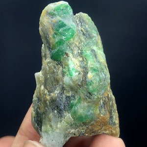 May include: A rough, green and brown rock with emerald crystals embedded in it. The rock is about the size of a fist.