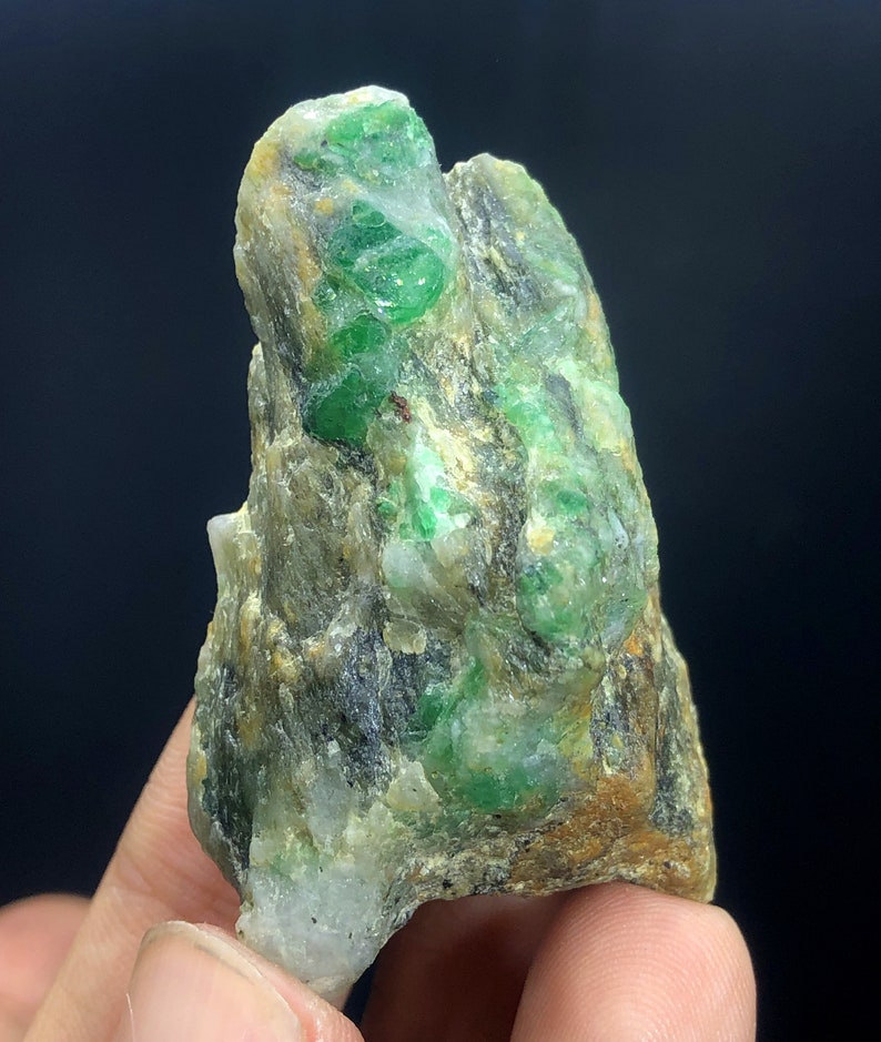 May include: A rough, green and brown rock with emerald crystals embedded in it. The rock is about the size of a fist.
