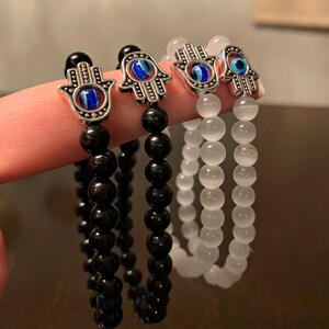 Puede incluir: Tres pulseras con dijes de mano de hamsa y cuentas de ojo turco. Las pulseras est&aacute;n hechas con cuentas de &oacute;nix negro, cuentas de &aacute;gata blanca y cuentas de &aacute;gata blanca.
