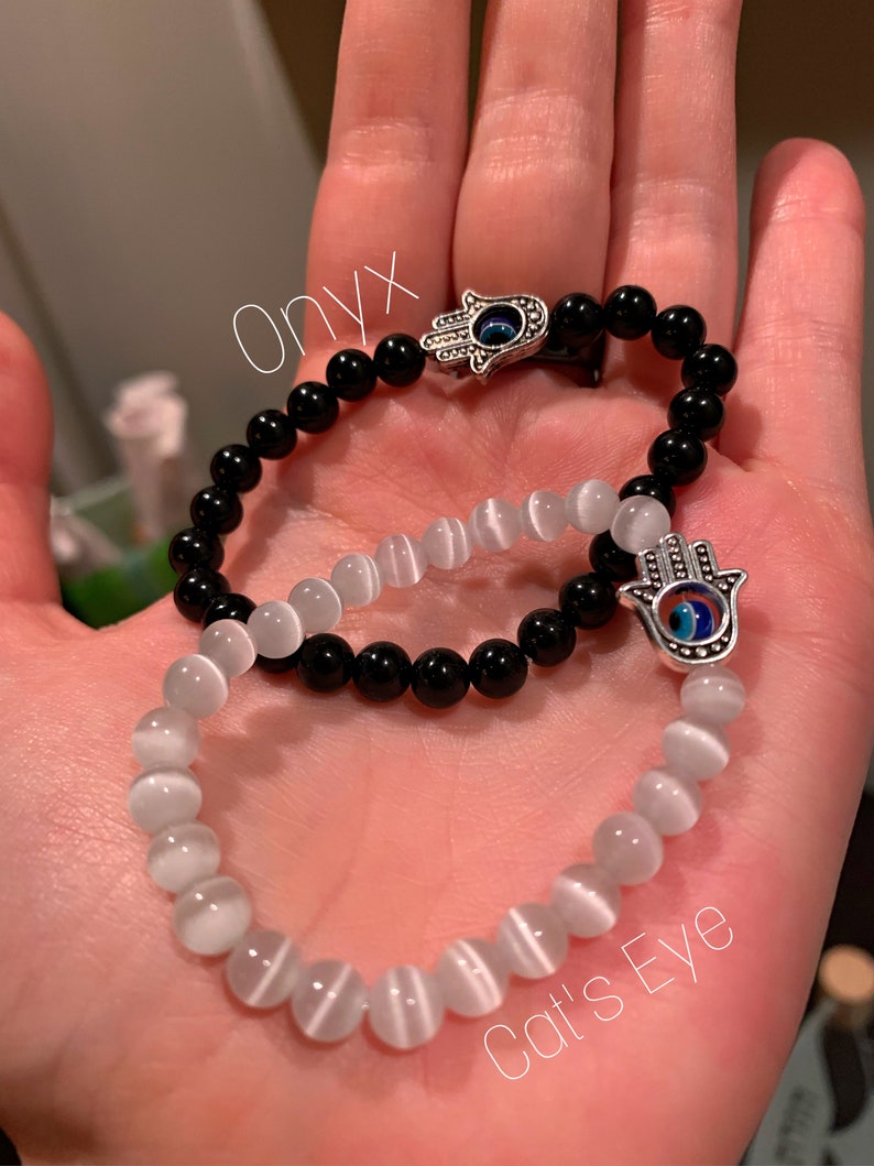 Puede incluir: Dos pulseras con dijes de mano de hamsa. Una pulsera est&aacute; hecha de cuentas de &oacute;nix negro y la otra de cuentas de ojo de gato blanco.