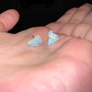 May include: A pair of iridescent opal earrings with silver posts. The opals are irregular in shape and have a light blue and white colour.