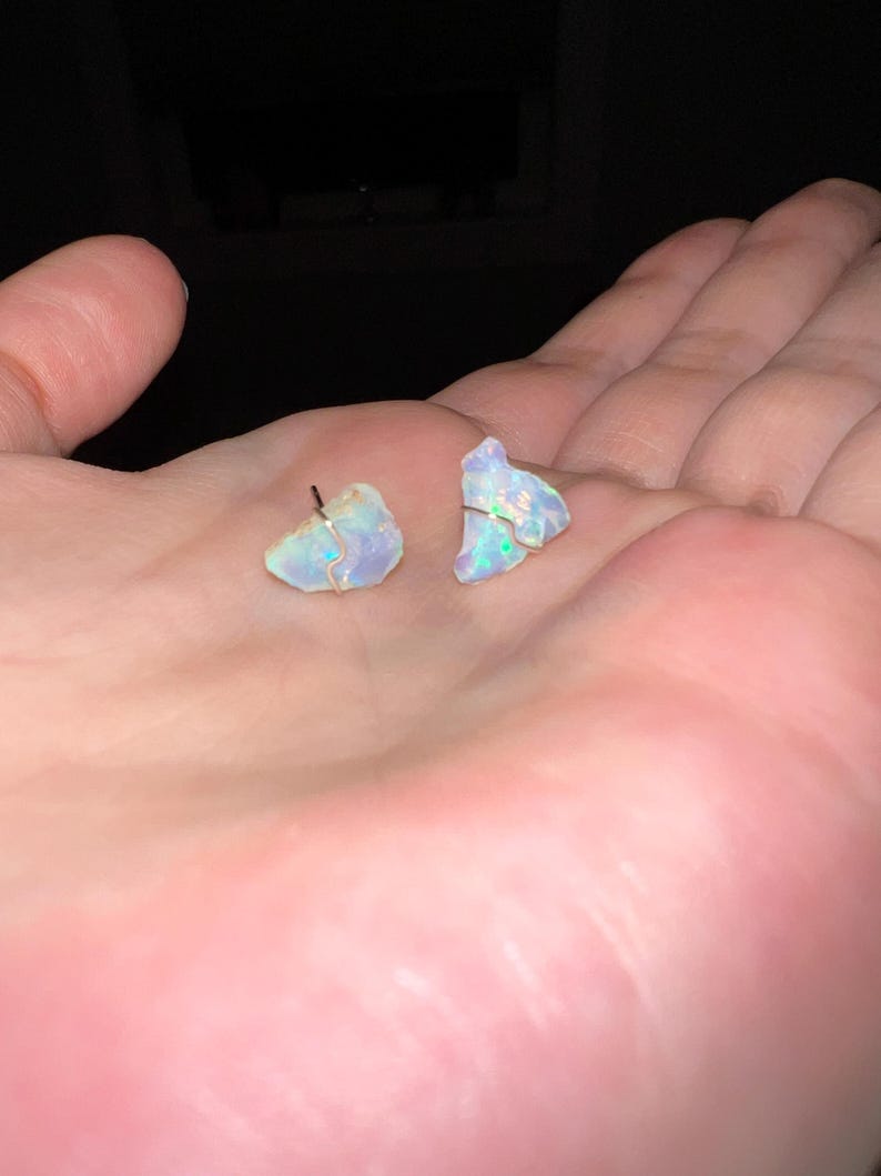 May include: A pair of iridescent opal earrings with silver posts. The opals are irregular in shape and have a light blue and white colour.
