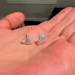 May include: A pair of iridescent opal earrings with silver posts. The opals are irregular in shape and have a milky white colour with flashes of blue, green, and pink.