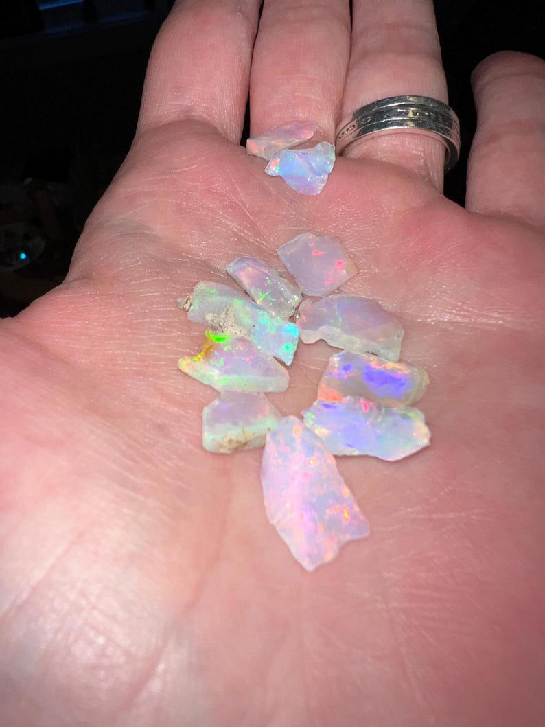 May include: A collection of small, iridescent opal gemstones in various shapes and sizes. The opals are a pale white with flashes of rainbow colours.