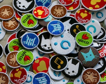 May include: A collection of colorful embroidered patches featuring various designs, including musical notes, cats, and geometric patterns. The patches are circular and have white stitching around the edges.