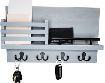 May include: A gray wooden wall organizer with a shelf, mail slots, and four black hooks. A black wallet rests on the shelf, and keys hang from the hooks. The organizer is painted in a light gray color.