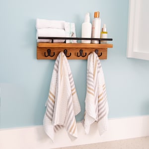 May include: A wooden shelf with black metal hooks and a black metal rail. There are two white towels with brown stripes hanging on the hooks. There are also several bottles of toiletries on the shelf.