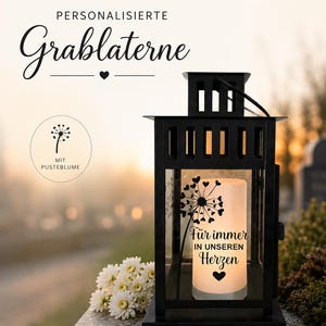 Könnte beinhalten: Schwarze Metall-Grablaterne mit rechteckiger Basis und Griff. Die Laterne hat eine Glasscheibe mit dem Schriftzug "Für immer in unseren Herzen" und einem Pusteblumen-Design. Weiße Blumen sind links.