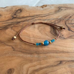 May include: A brown string bracelet with a blue gemstone and gold accents.