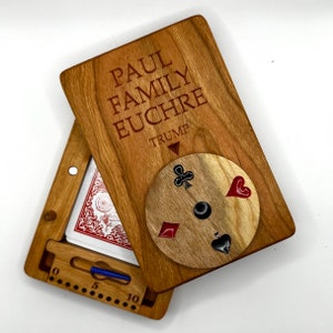 May include: A wooden box with a hinged lid, engraved with "PAUL FAMILY EUCHRE TRUMP". The lid is open, revealing a card game scoring board and a spinning wheel with four card suits.