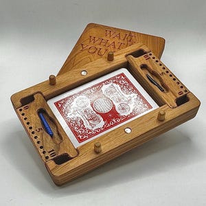 May include: A wooden box game with the words "Wait What You" engraved on the lid. The box is open and a playing card is visible inside. The card has a red and white design with a globe and two motorcycles.