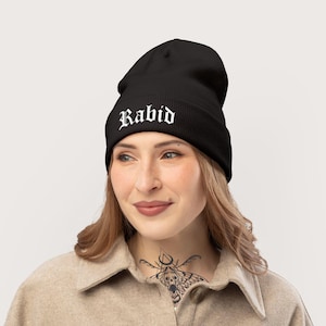 May include: Black beanie with the word "Rabid" in white gothic lettering. The hat is made of a soft material and is designed to be worn on the head. The beanie is a stylish accessory for cold weather.