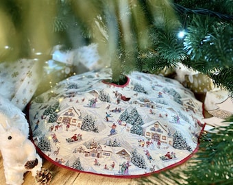 May include: A white and red Christmas tree skirt with a winter village scene. The skirt features a snowy landscape with houses, trees, and people skiing and snowboarding.