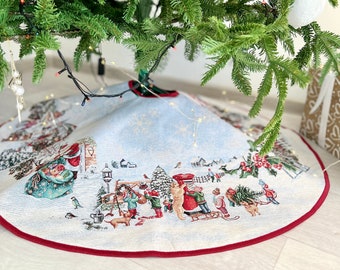 May include: A white and blue Christmas tree skirt with a red border. The skirt features a winter scene with children, animals, and a house.