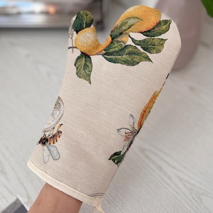 May include: A beige oven mitt with a lemon tree design. The mitt features yellow lemons, green leaves, and a bee.