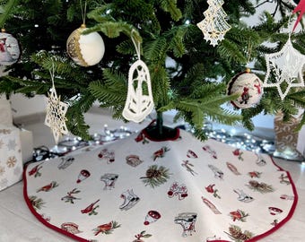 May include: A white Christmas tree skirt with a red trim. The skirt features a repeating pattern of ice skates, birds, pine cones, and holly berries.